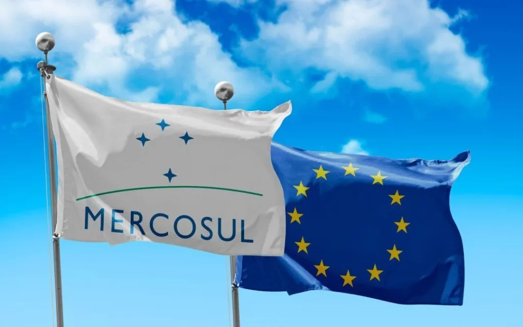 Na imagem aparece as bandeiras do Mercosul e da União Europeia, representando o Acordo Mercosul-UE